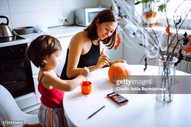 charming woman and cute little girl passionately paint pumpkin together in cozy kitchen - paint branch stock pictures, royalty-free photos & images