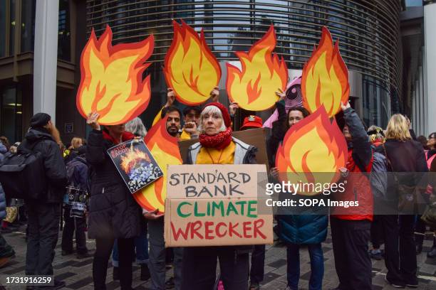 Protester holding a placard calling Standard Bank a 'climate wrecker' stands with protesters holding cardboard cutouts resembling fire during the...