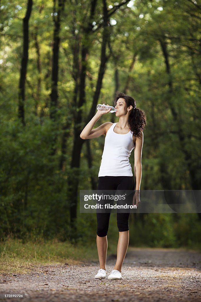 Joven mujer agua potable en el parque
