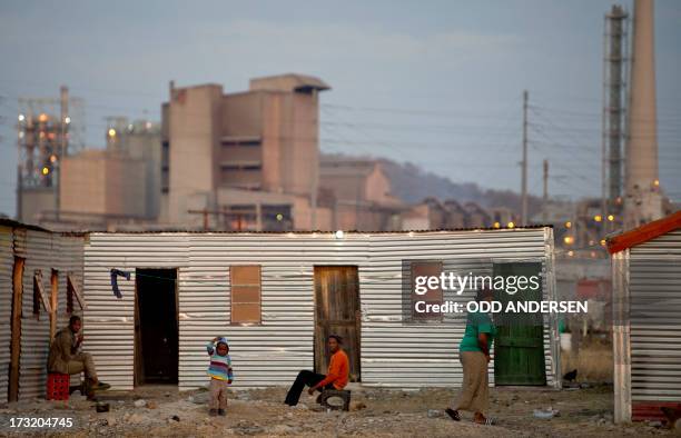 People sit outside their shacks on July 9, 2013 in the Nkaneng shantytown next to the platinum mine, run by British company Lonmin, in Marikana. On...