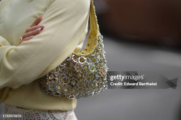 Guest wears a pastel yellow bag with attached structure made of metallic circles, outside Rabanne, during the Womenswear Spring/Summer 2024 as part...