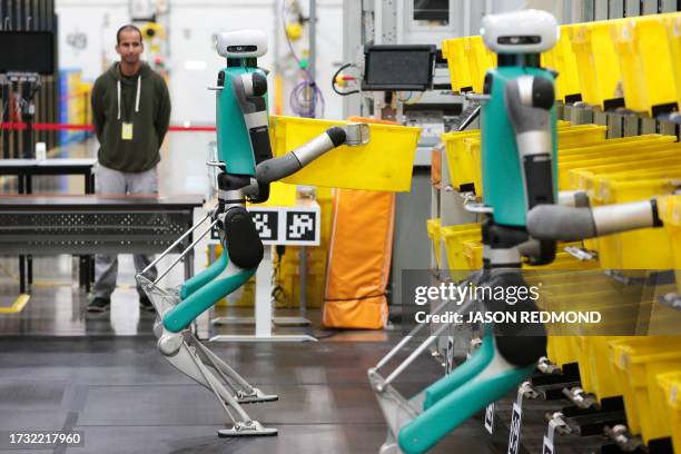 Bipedal robots in testing phase move containers during a mobile-manipulation demonstration at Amazon's "Delivering the Future" event at the company's...