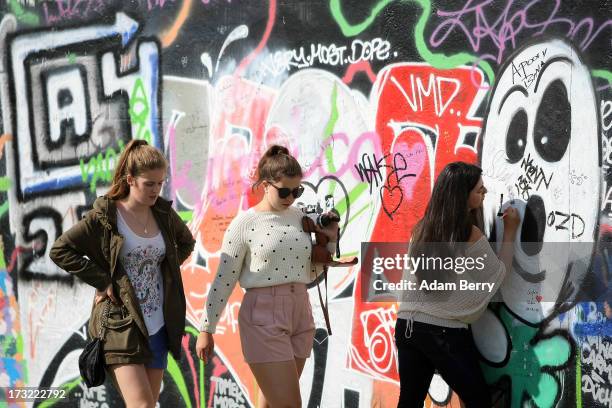 Tourist writes graffiti on the opposite side of the East Side Gallery section of the former Berlin Wall on July 10, 2013 in Berlin, Germany. The...