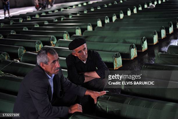 Bosnian Muslims, survivors of Srebrenica 1995 massacre, pray and cry near body caskets of their relatives, layed out in a factory hangar, near...