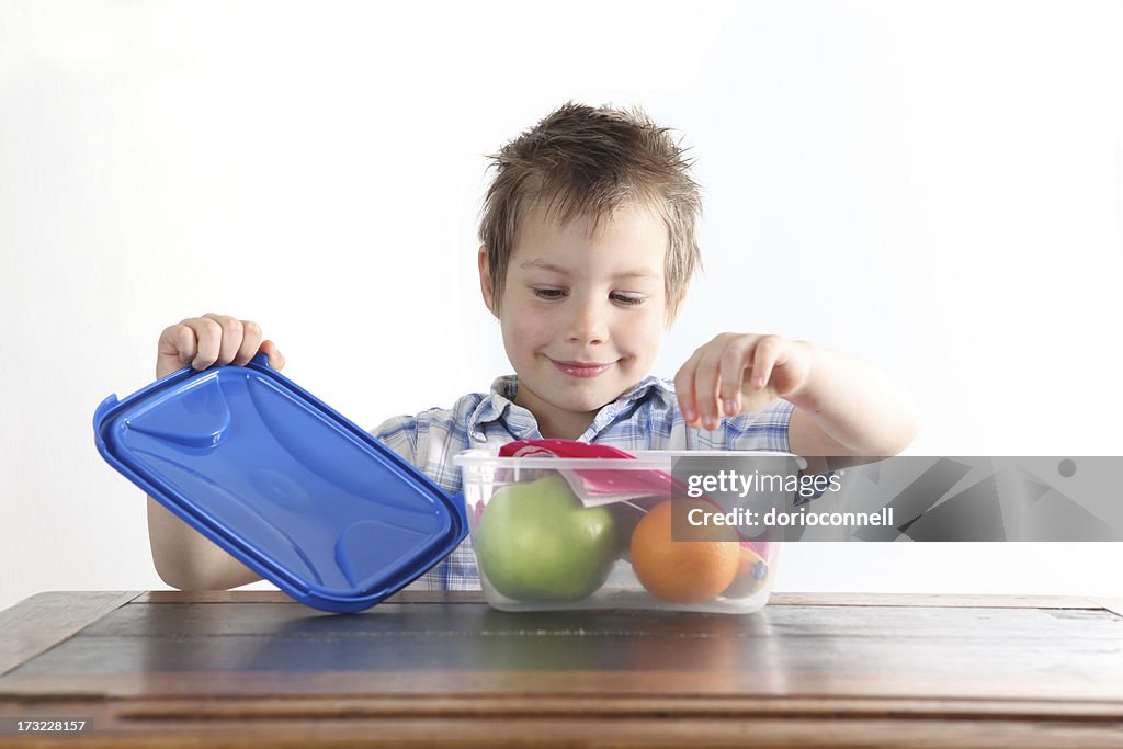 A boy opens a Tupperware box with an apple and orange inside