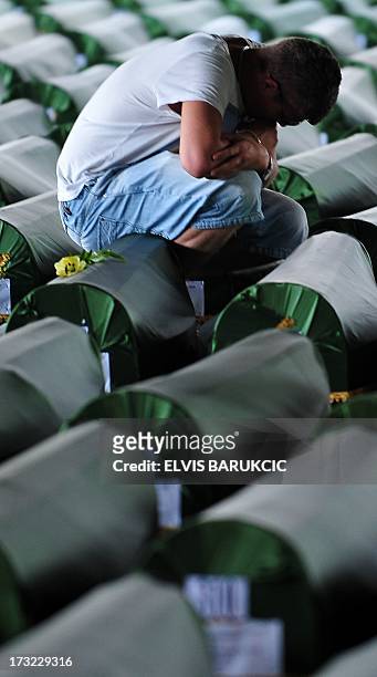 Bosnian Muslim man, survivor of Srebrenica 1995 massacre, mourns near the body casket of his relative, layed out in a factory hangar, near memorial...