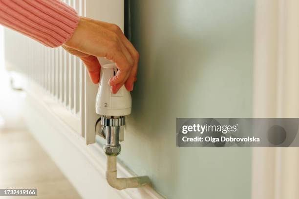 a woman's hand adjusting temperature on a heating radiator - radiator stockfoto's en -beelden