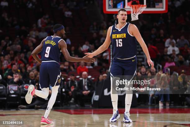 Justin Holiday of the Denver Nuggets high fives Nikola Jokic against the Chicago Bulls during the first half at the United Center on October 12, 2023...
