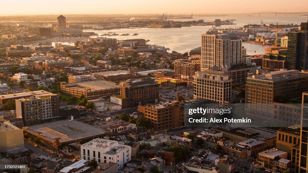 Real estate in riverfront city. Baltimore, MD Residential District and waterfront in dawn. Sunny urban skyline and harbor in the distance