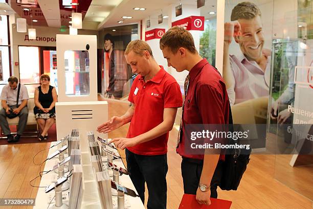 An employee, center, demonstrates a smartphone to a customer inside an OAO Mobile TeleSystems retail outlet in Moscow, Russia, on Thursday, July 11,...