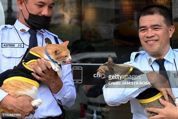 Security guards hold cats Shangki and Laura outside a fast food chain in Quezon City on September 27, 2023. A cat wearing a black-and-yellow security...