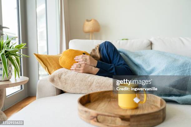 woman hiding her face while lying on sofa in the living room - gesicht verstecken stock-fotos und bilder