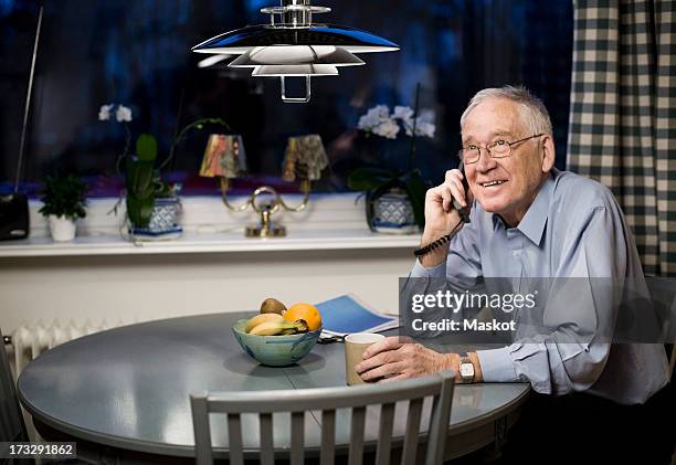 happy senior looking up while using telephone at dining table - festnetztelefon stock-fotos und bilder