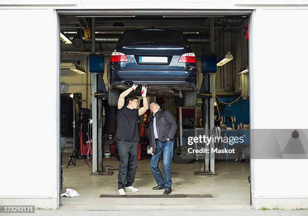 young mechanic explaining car problems to customer at auto repair shop - auto interieur stockfoto's en -beelden
