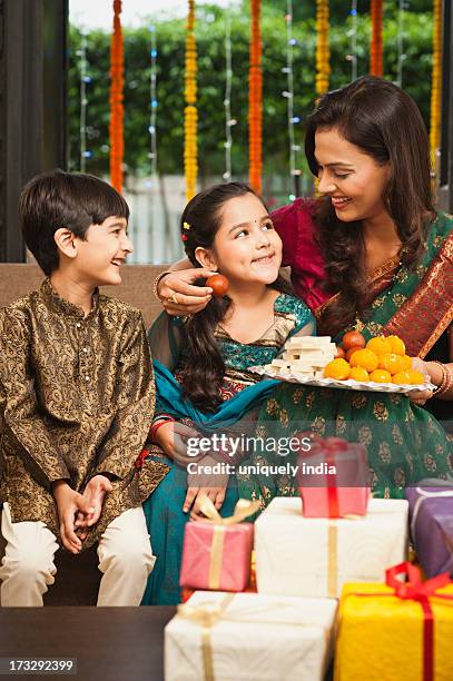 woman feeding gulab jamun to her daughter on diwali - diwali family stock pictures, royalty-free photos & images