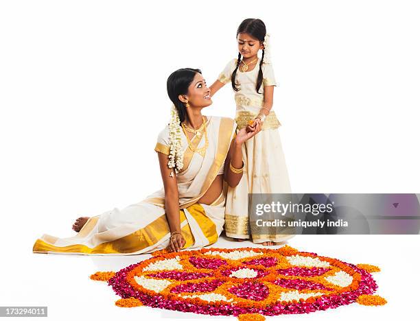 south indian woman making a rangoli of flowers with her daughter at onam - onam foto e immagini stock