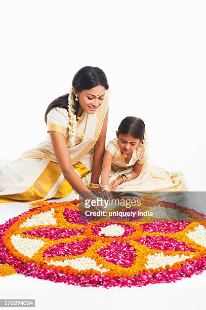 south indian woman making a rangoli of flowers with her daughter at onam - indian kolam stock-fotos und bilder