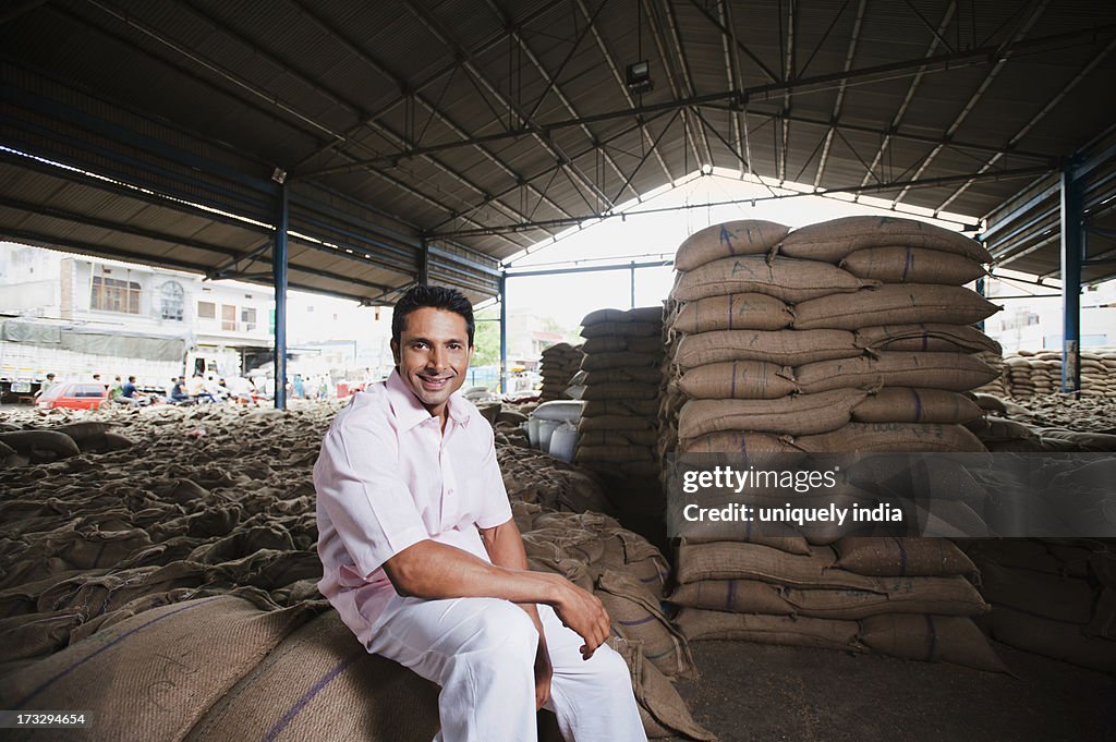 Man sitting on stack of wheat sacks in a warehouse, Anaj Mandi, Sohna, Gurgaon, Haryana, India