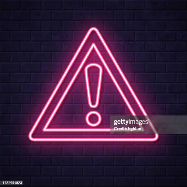 hazard warning attention. glowing neon icon on brick wall background - warning symbol stock illustrations