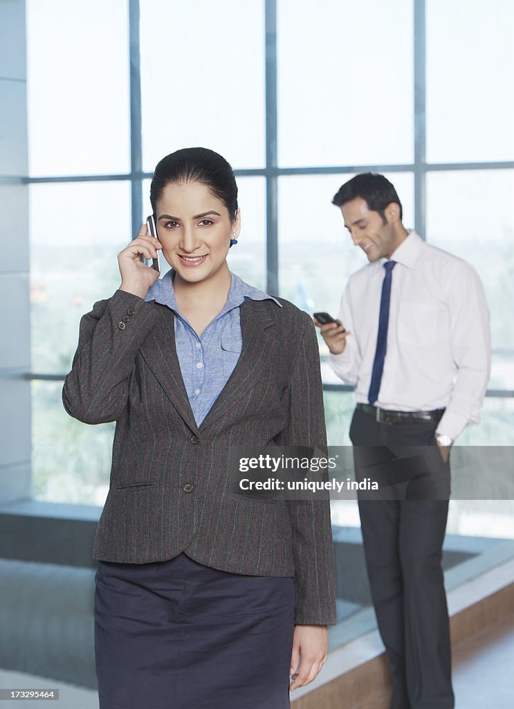 Businesswoman talking on a mobile phone with her colleague in the background