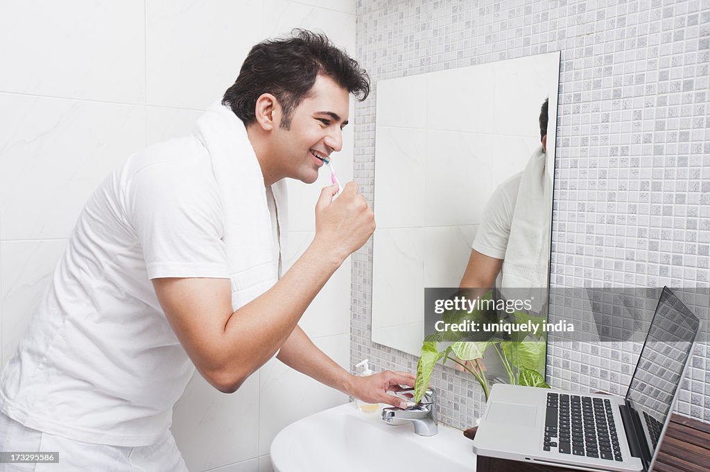 Man using a laptop while brushing his teeth