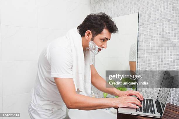 man using a laptop while shaving his face - sud side company stock pictures, royalty-free photos & images