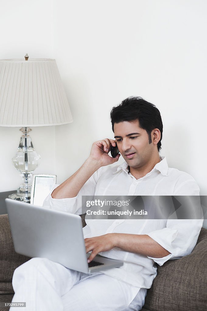 Man talking on mobile phone and using laptop