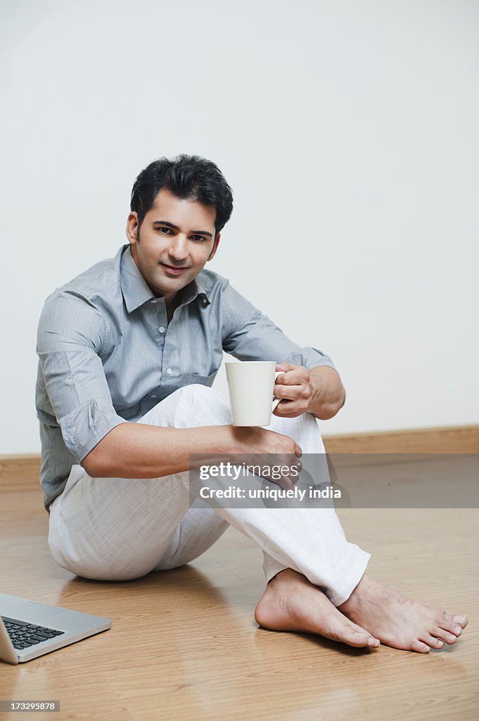 Man drinking coffee with a laptop beside him