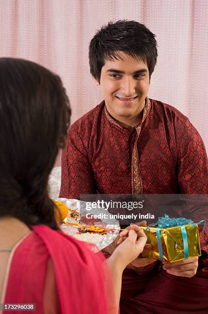 man holding a gift while his sister holding a puja thali at raksha bandhan - rakhi stock pictures, royalty-free photos & images