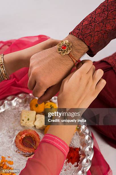 teenage girl tying rakhi on her brother wrist - rakhi stock pictures, royalty-free photos & images