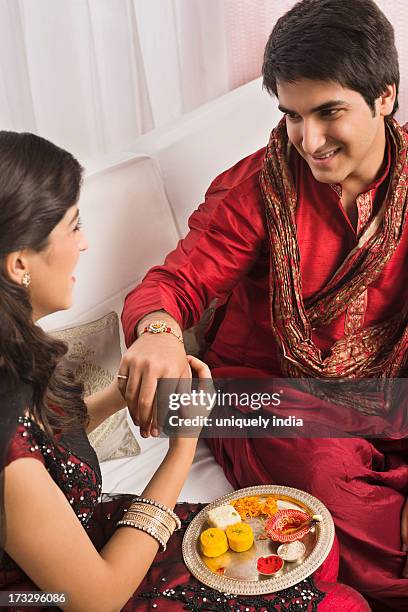 teenage girl tying rakhi on her brother wrist - rakhi stock pictures, royalty-free photos & images