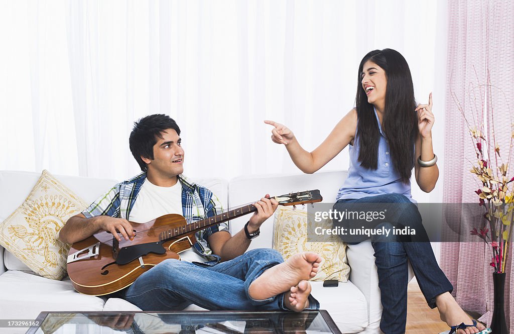 Man playing a guitar with his sister sitting besides him