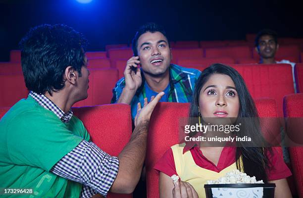 couple watching movie while a man talking on cell phone in a cinema hall - indian couple in theaters stock pictures, royalty-free photos & images