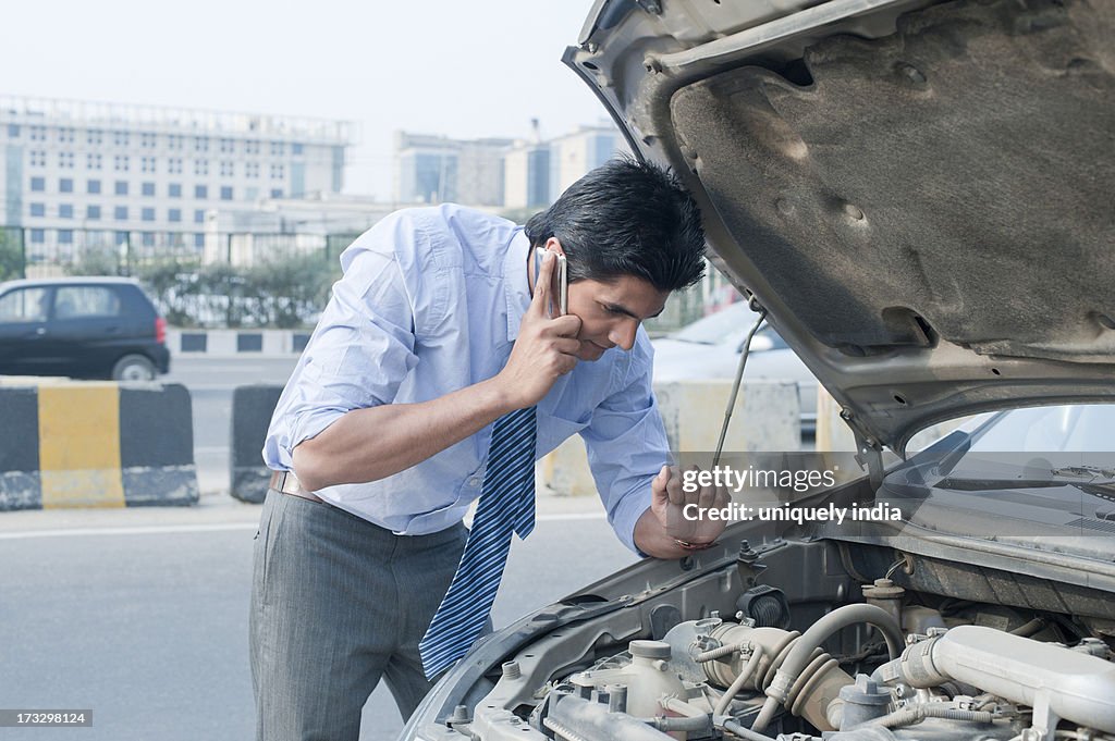 Businessman using a mobile phone near a broken down car, Gurgaon, Haryana, India