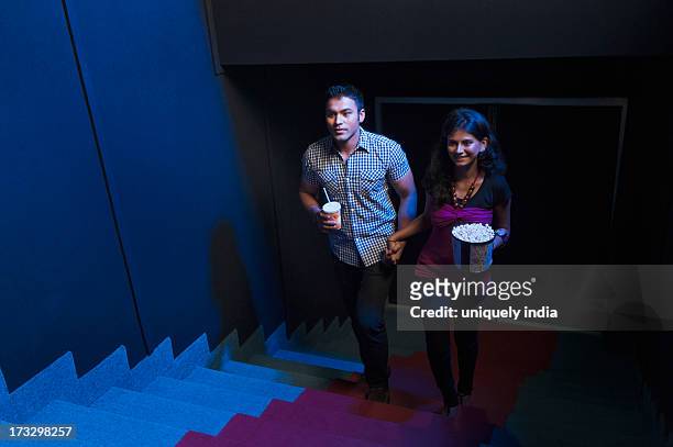couple moving up on steps in a cinema hall - indian couple in theaters stock pictures, royalty-free photos & images