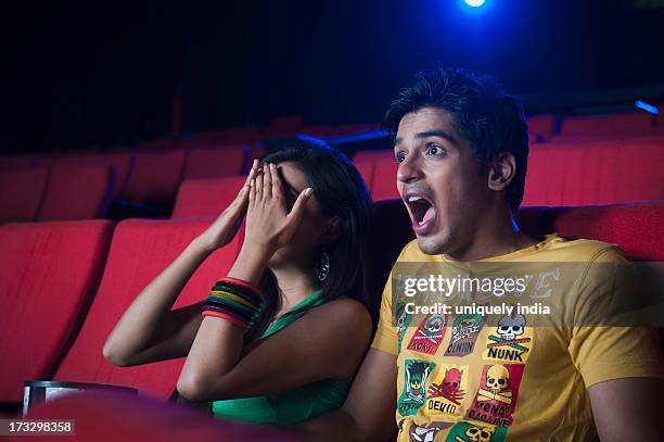 couple watching movie and looking surprised in a cinema hall - indian couple in theaters - fotografias e filmes do acervo