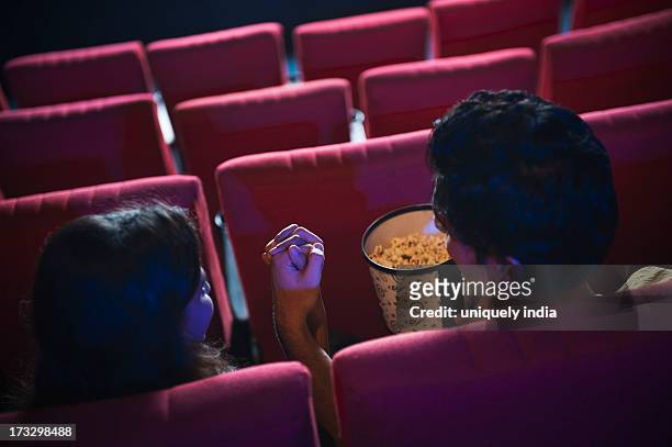 couple enjoying movie with popcorns in a cinema hall - indian couple in theaters stock pictures, royalty-free photos & images