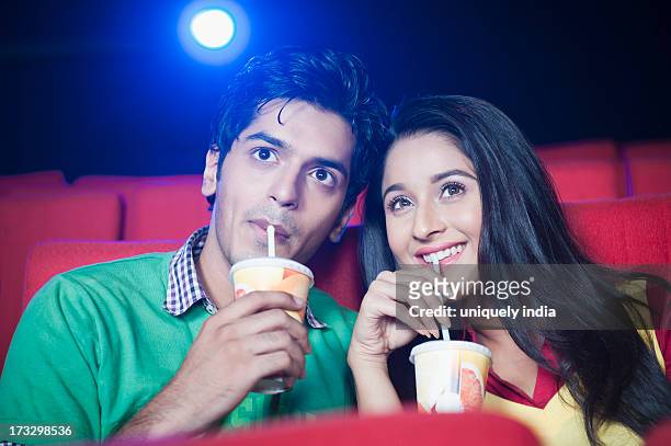 couple enjoying soft drinks while watching movie in a cinema hall - indian couple in theaters stock pictures, royalty-free photos & images