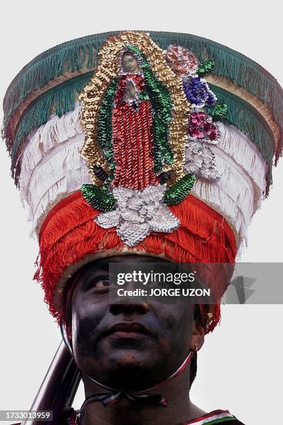 Man, with his face painted in black, is dressed like a Mexican Indigenous soldier and wears a hat with the image of the Virgin of Guadalupe, during...