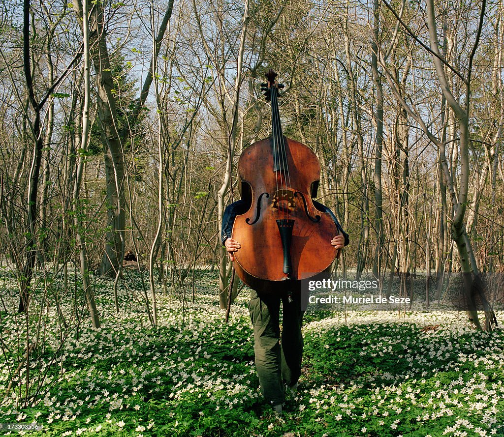 Woman carrying cello through wood