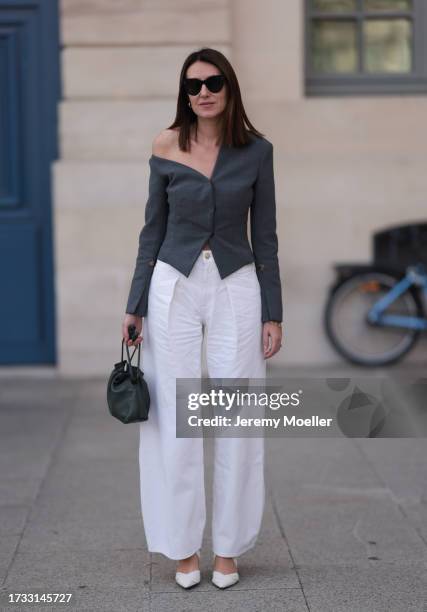 Guest seen wearing black sunglasses, grey suit jacket offshoulder, white wide suit pants with a golden button and a green leather handbag and white...