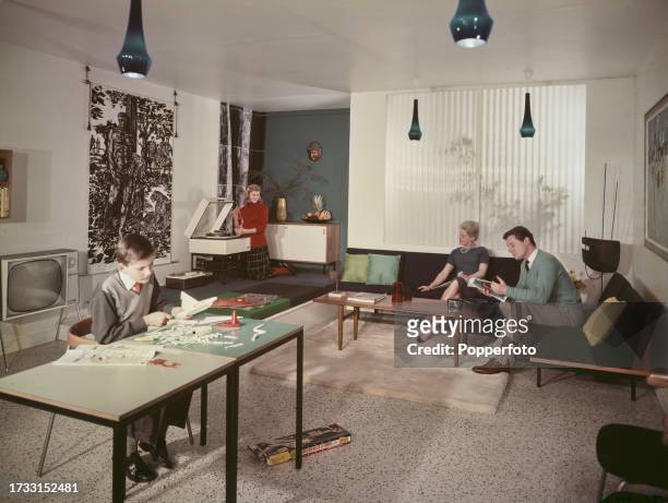 Family relax in the contemporary styled living room of their modern house in England in July 1960. The boy assembles a kit of a model jet bomber, the...