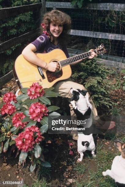 American actress Linda Blair playing guitar in the garden of her mother's house in Westport, Connecticut, June 15th 1977. Her Jack Russell terriers...