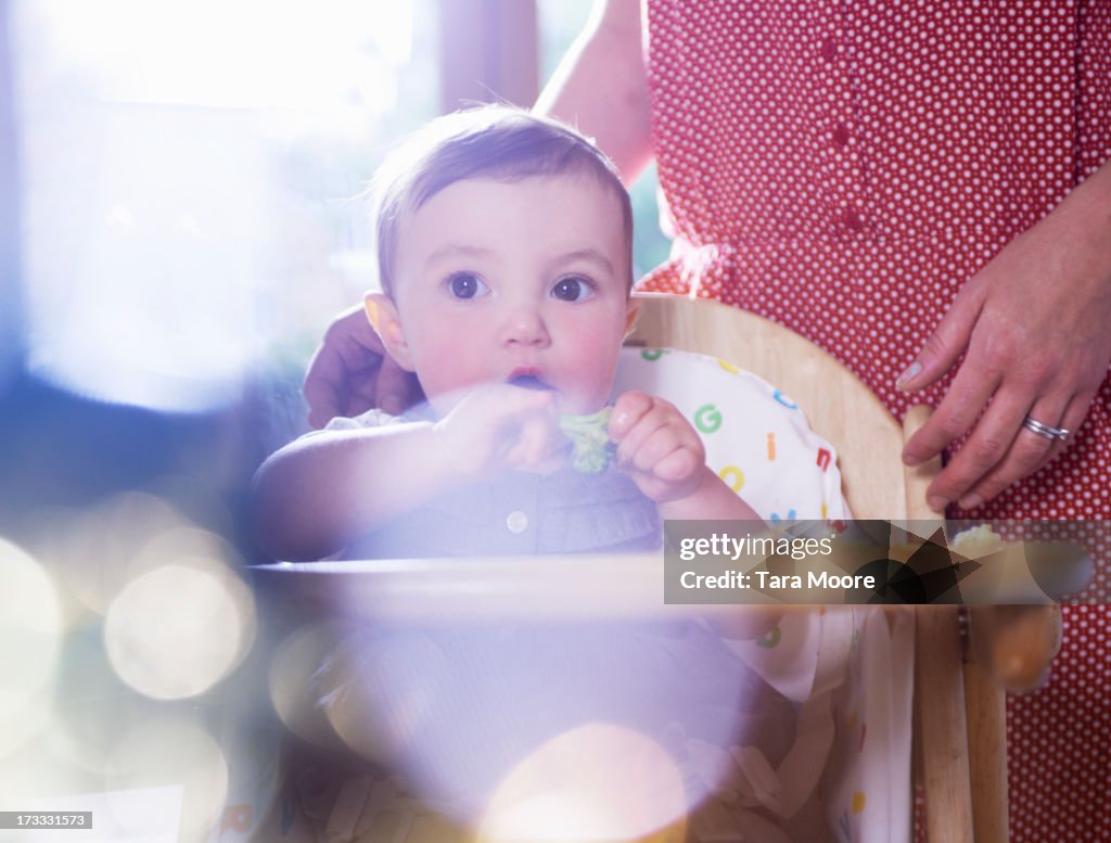 Baby eating broccoli in high chair