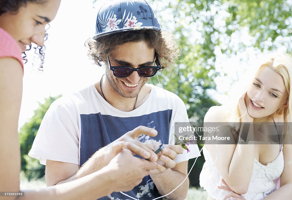 Friends sharing headphones and mobile in park