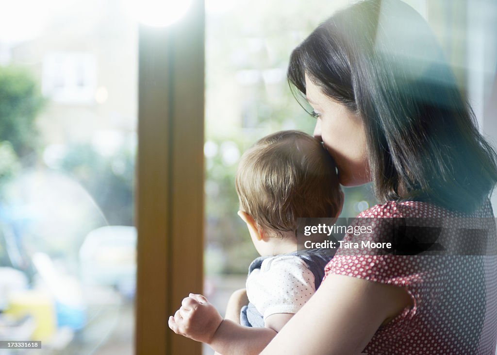 Mother holding toddler and looking out window