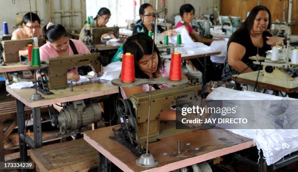 Women work at a sweatshop sewing clothes under contract with local clothing manufacturers in Manila on July 12, 2013. Visiting World Bank vice...