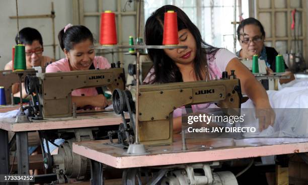 Women work at a sweatshop sewing clothes under contract with local clothing manufacturers in Manila on July 12, 2013. Visiting World Bank vice...