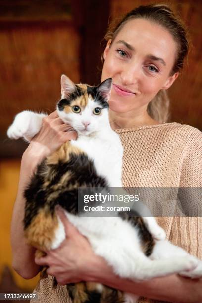 happy woman holding her adopted calico cat in her arms and smiling at camera - pet adoption stock pictures, royalty-free photos & images