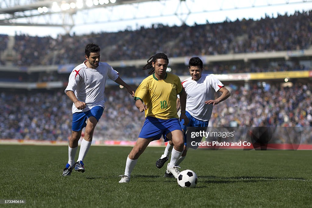 Three men playing soccer in stadium
